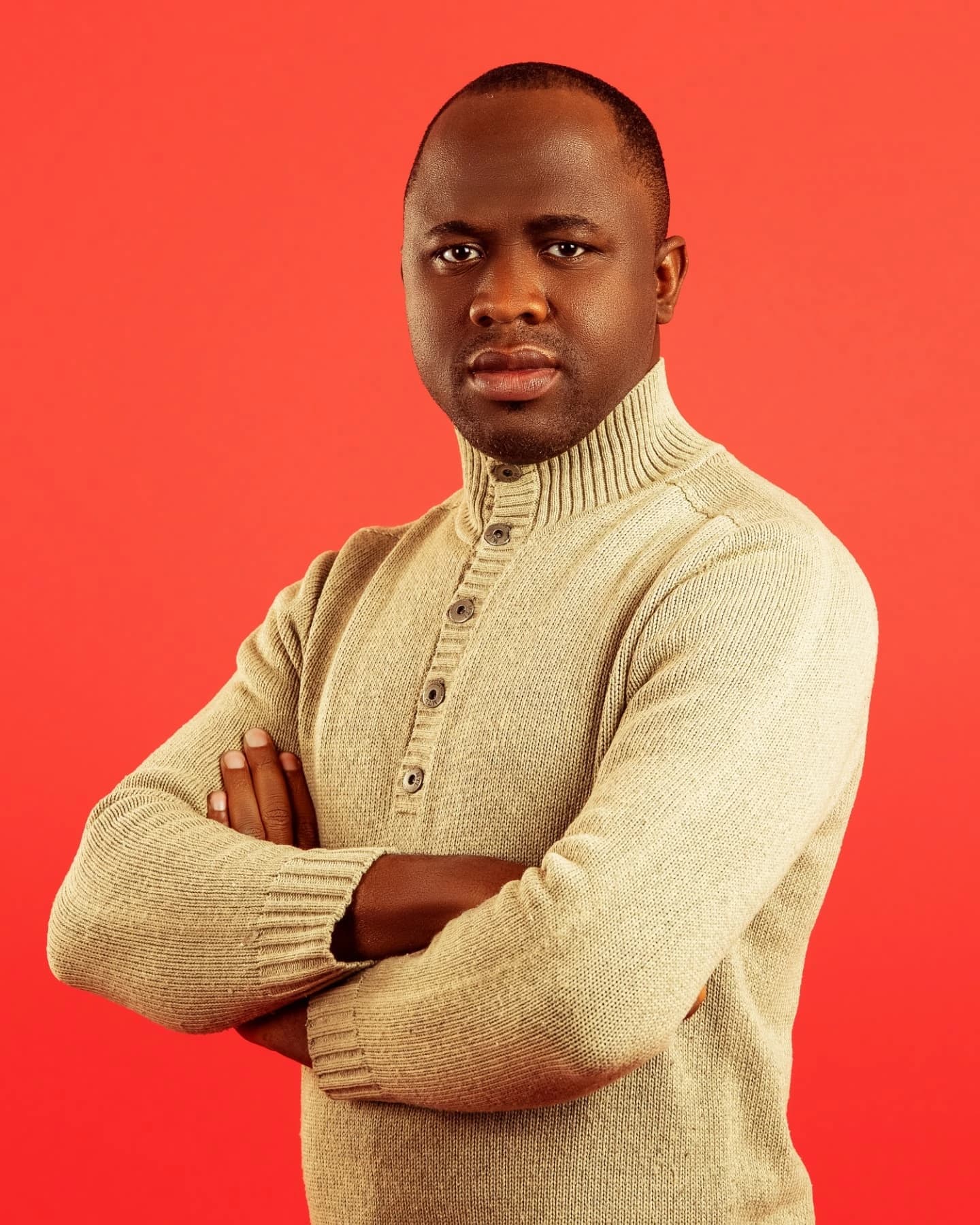 The photographer behind Precious Diamond, arms folded, in a cream jumper against a red backdrop